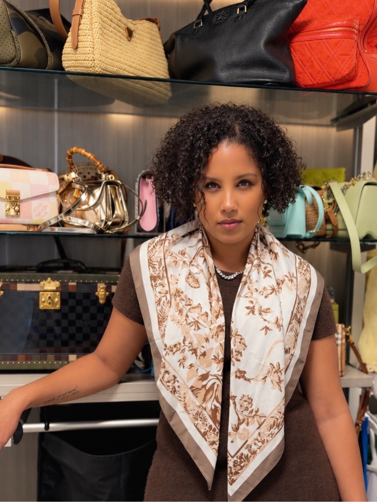 Juelle, personal stylist, standing in a finished client's closet in a brown dress and floral scarf, handbags shelved behind her.
